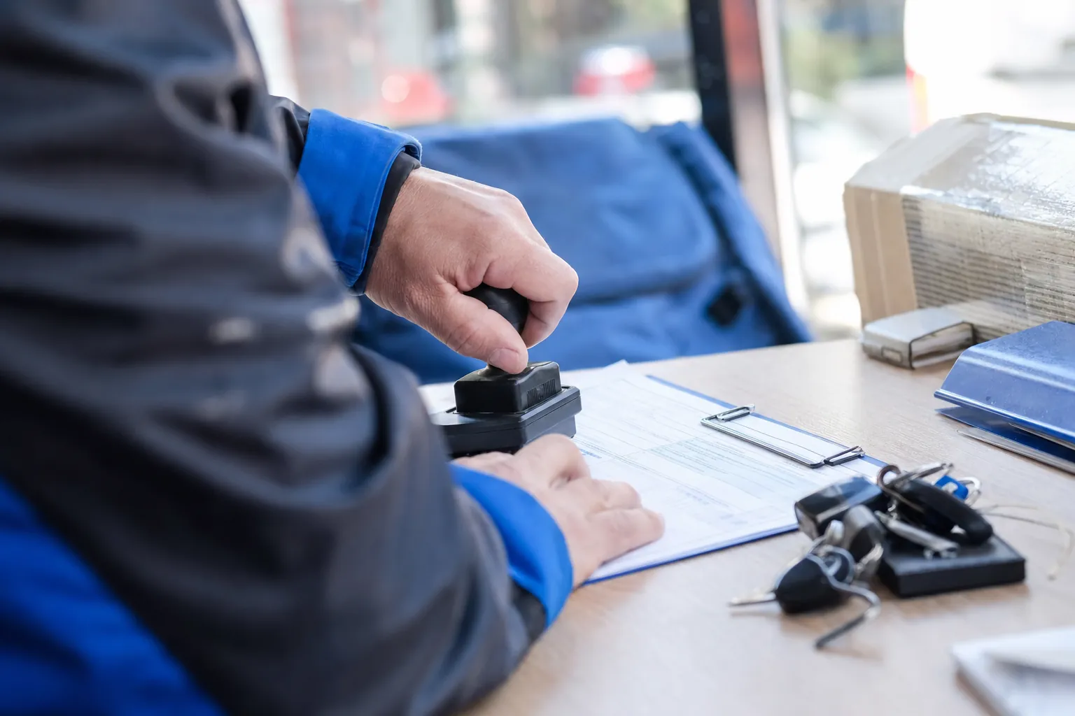 gros plan sur des mains posant un tampon d'encre sur une lettre de voiture papier, a cote d'un jeu de cles de camion