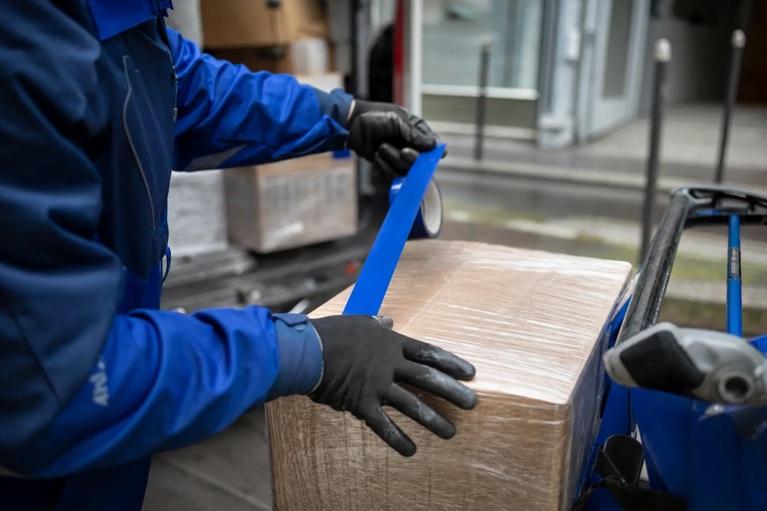 gros plan sur des mains gantees verifiant l'emballage et le film plastique d'un colis fragile, ruban de securite en cours